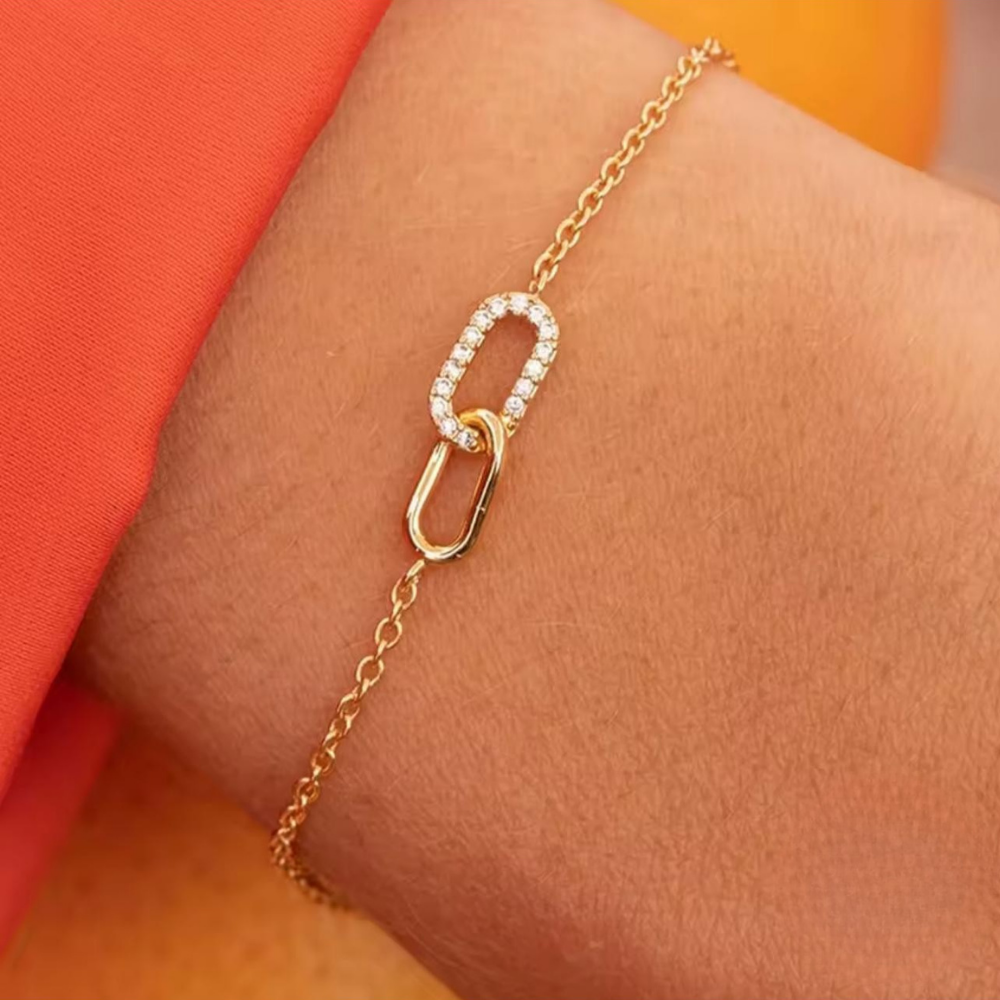 Gold bracelet with a diamond accent on a wrist against an orange background