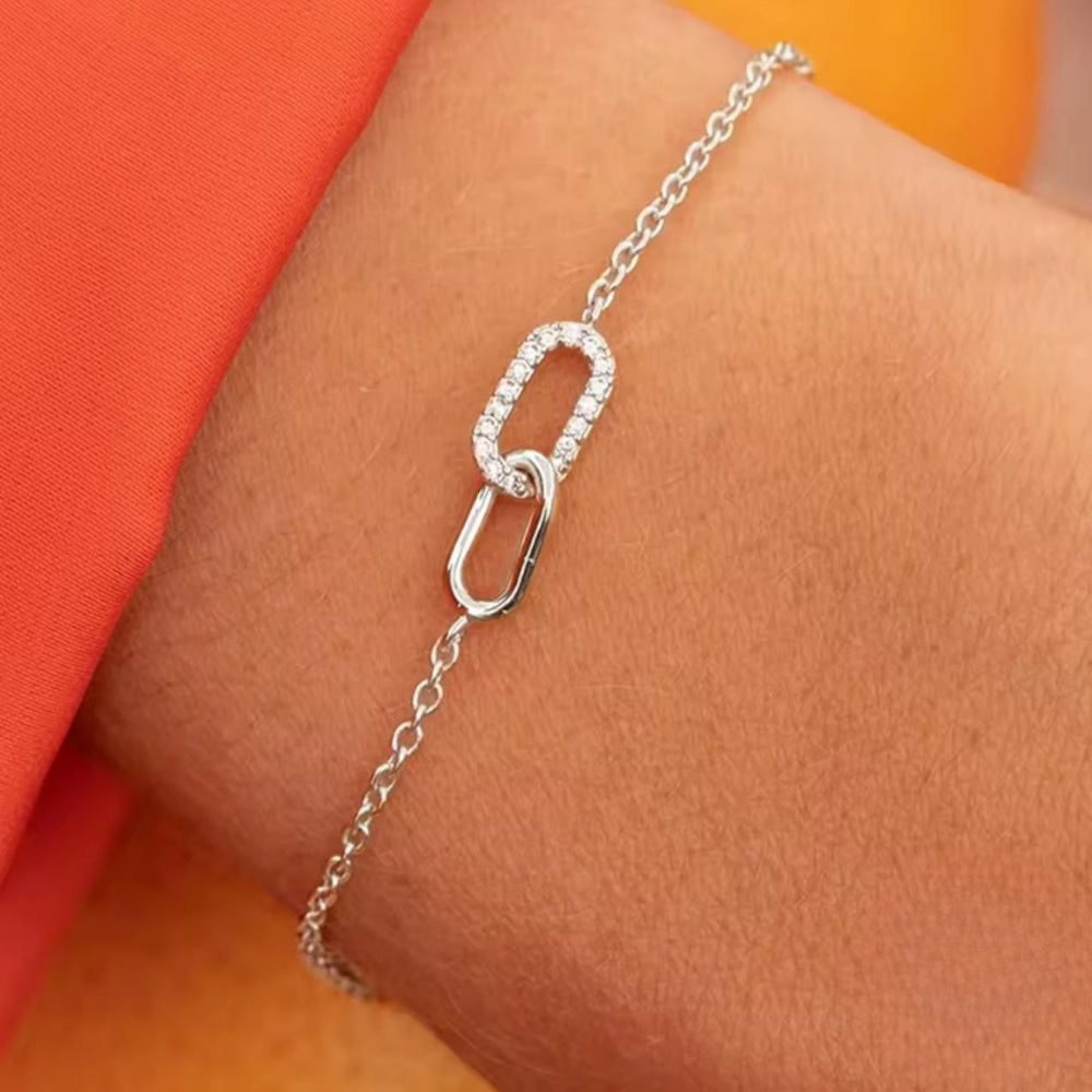 Silver bracelet with interlocking links on a wrist against an orange background