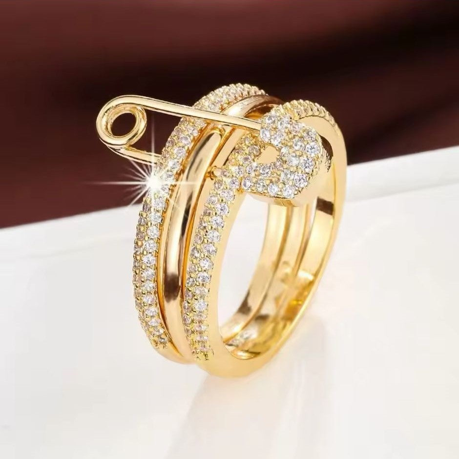 A gold-colored PinLock double band stainless steel ring with a safety pin design encrusted with dazzling stones.