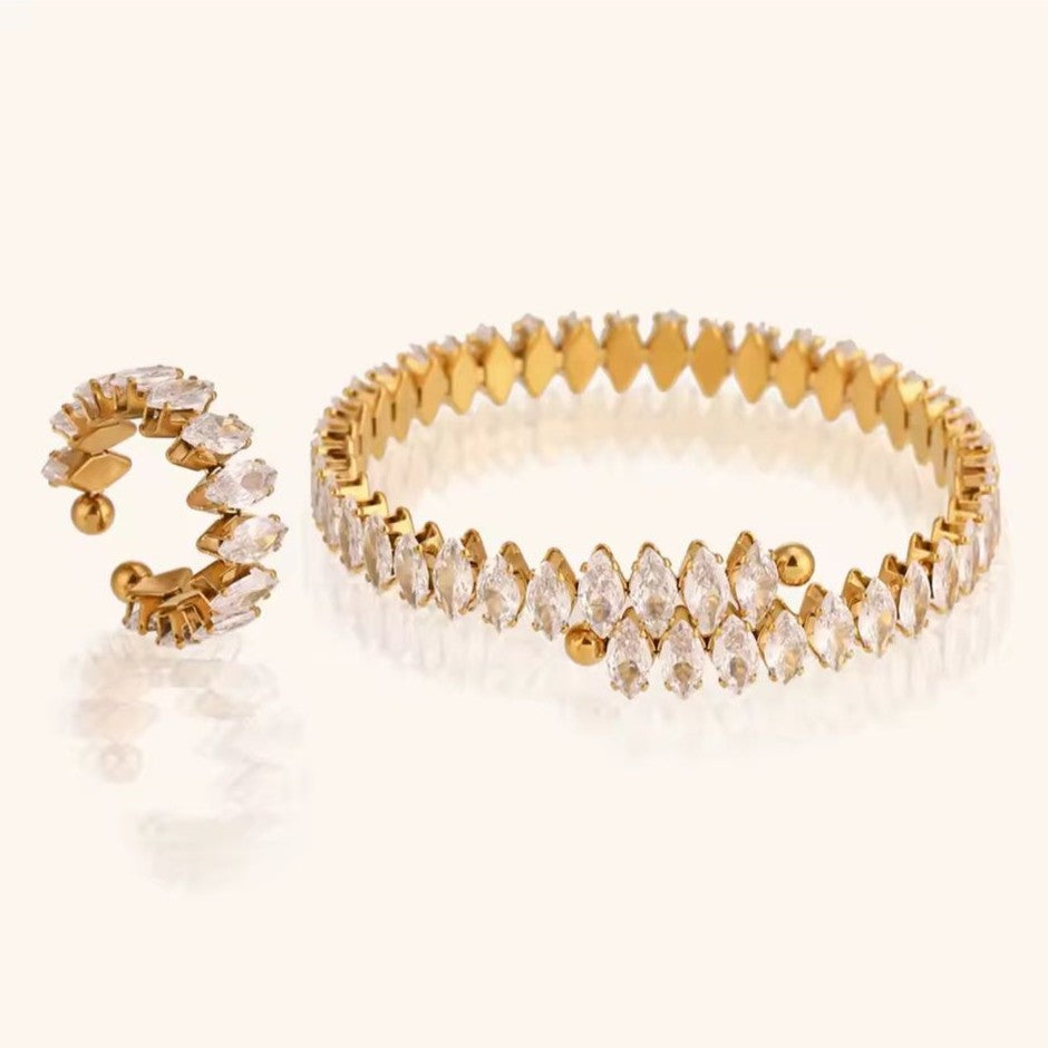 A pair of gold ring & bracelet with clear stones on a white background.