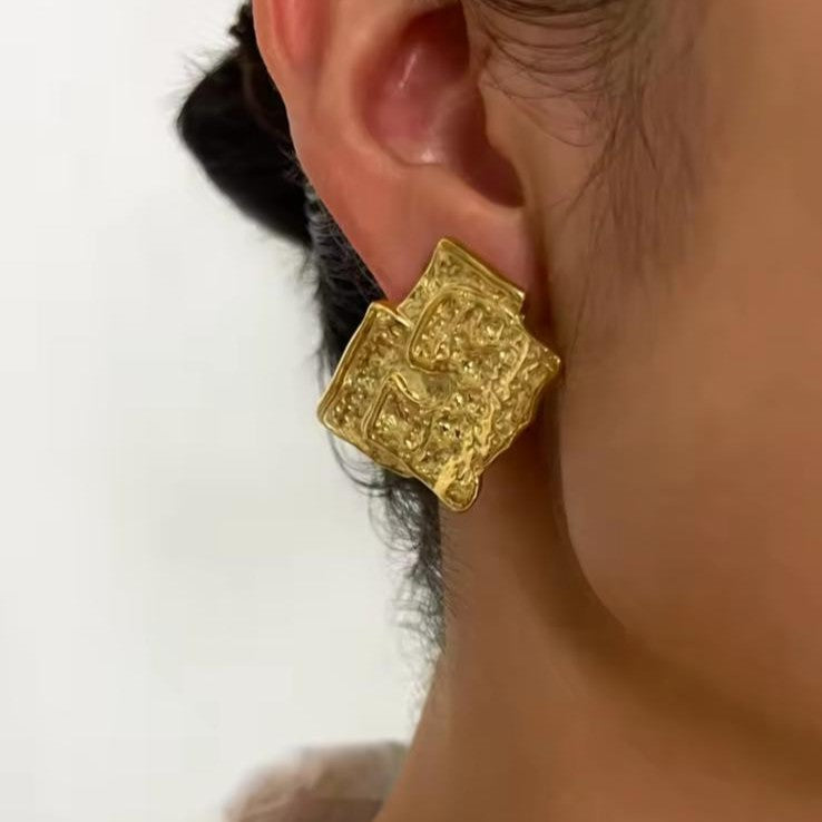 Gold earring worn on an ear with a neutral background