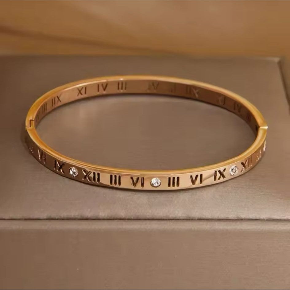 A Roman Style Stainless Steel Classic Bangle – Gold colored with white stones on a neutral background.