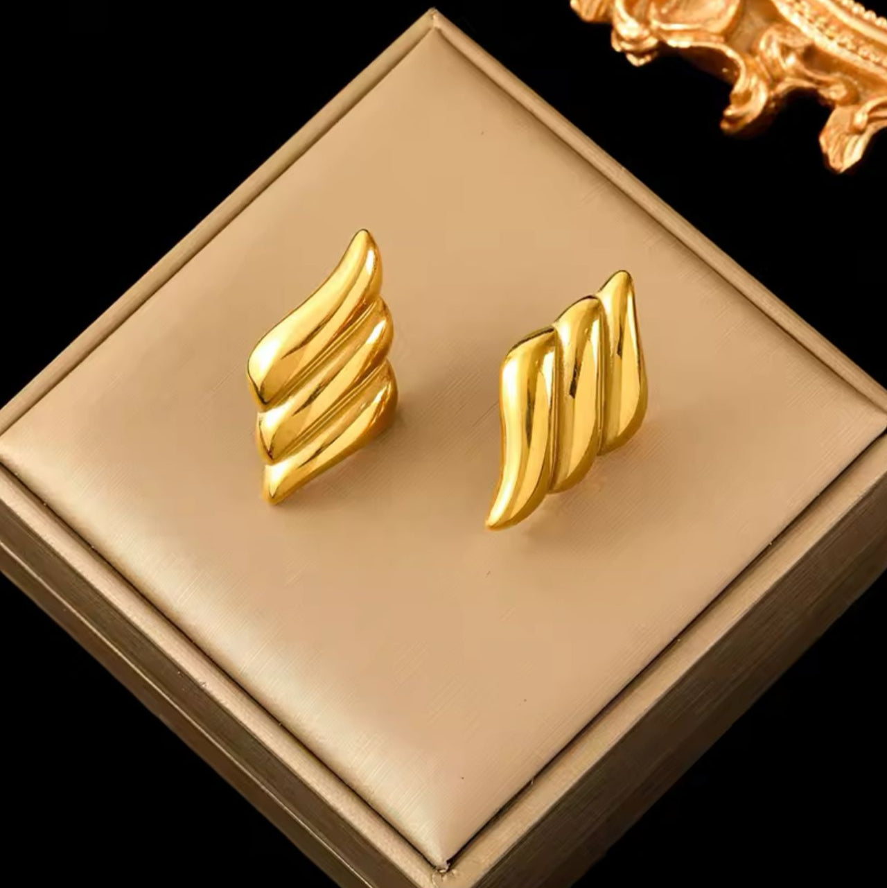 Gold wing-shaped earrings on a beige display box