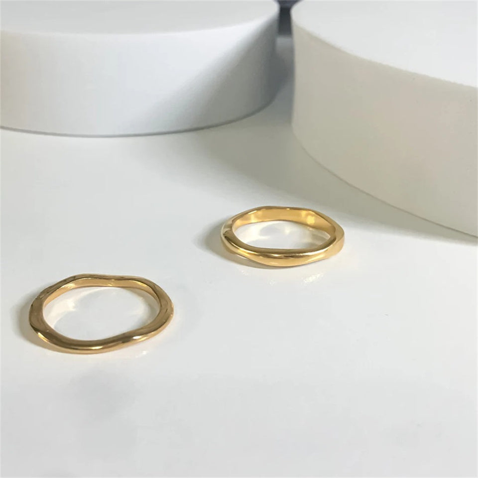 A pair of gold-colored band ring with a wavy design, made from stainless steel, displayed on a plain background.