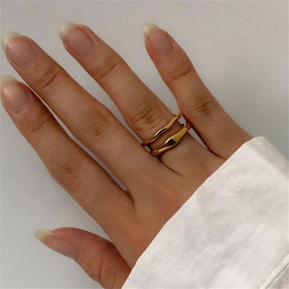 A gold-colored dual band ring with a wavy design, made from stainless steel, displayed on a plain background.