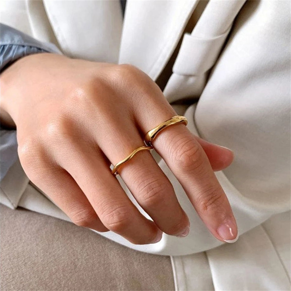 A gold-colored band ring with a wavy design, made from stainless steel, displayed on a hand.