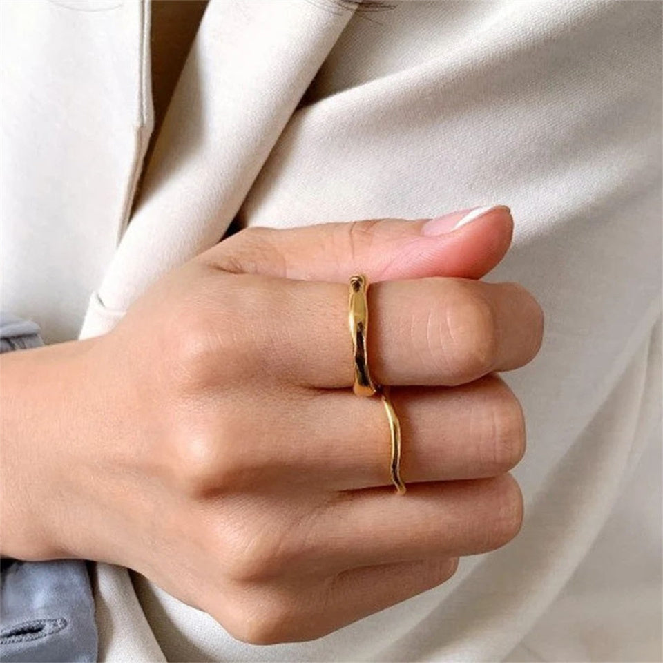 A gold-colored band ring with a wavy design, made from stainless steel, displayed on a hand.