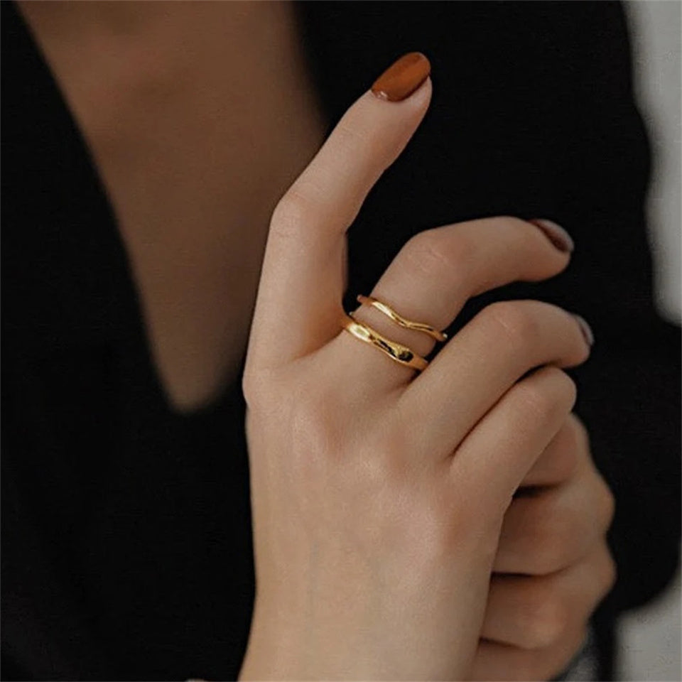 A gold-colored dual band ring with a wavy design, made from stainless steel, displayed on a hand.