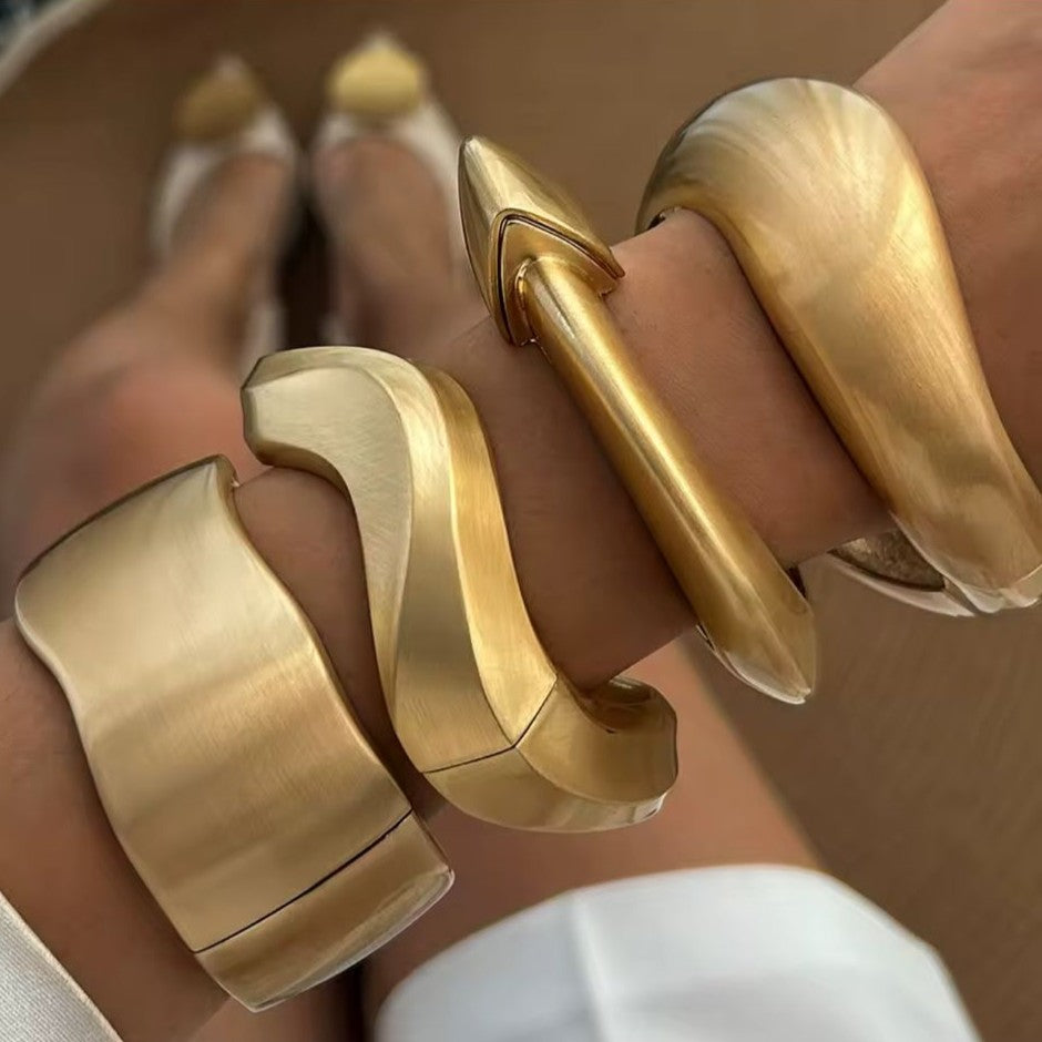 Gold bangles on a person's wrist with a neutral background