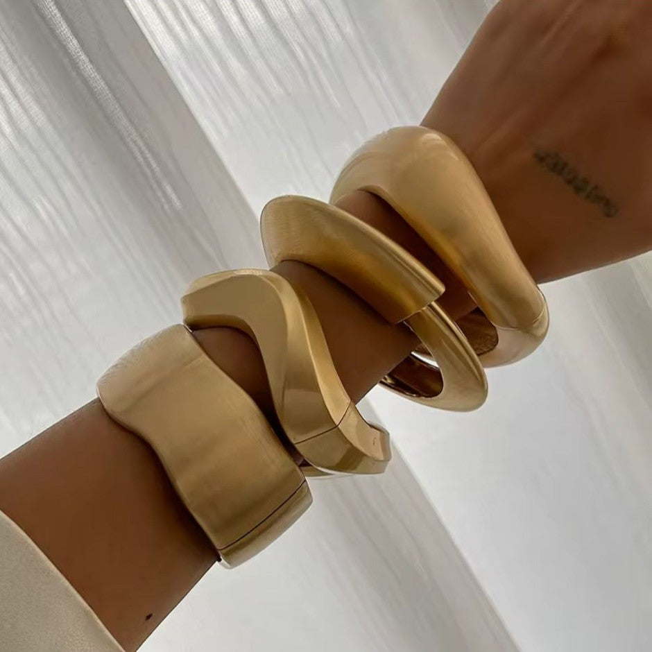 Close-up of a hand wearing three gold bangles against a neutral background