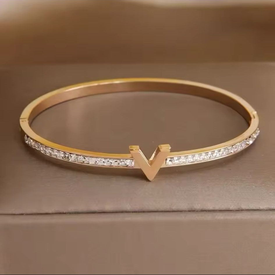 A gold stainless steel bracelet featuring a V-shaped pattern of inset stones, showcasing a sophisticated and elegant design.