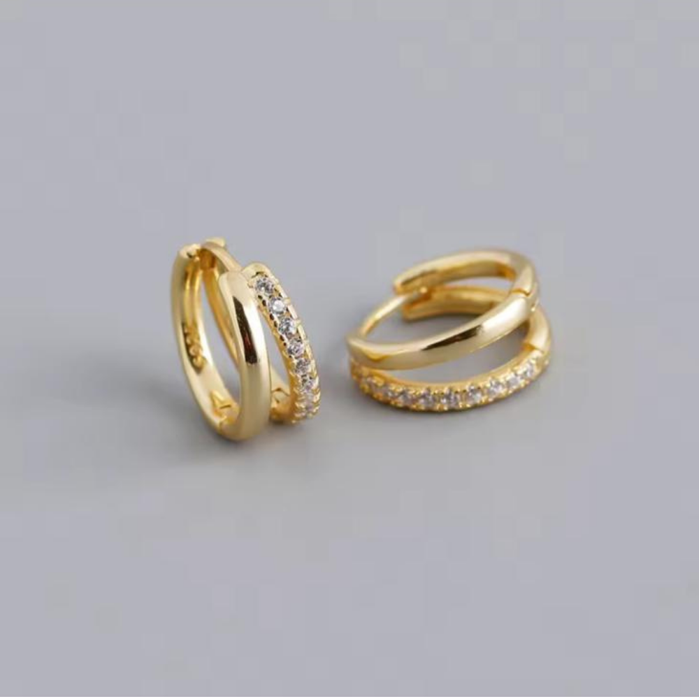 Two gold hoop earrings with embedded stones on a light gray background