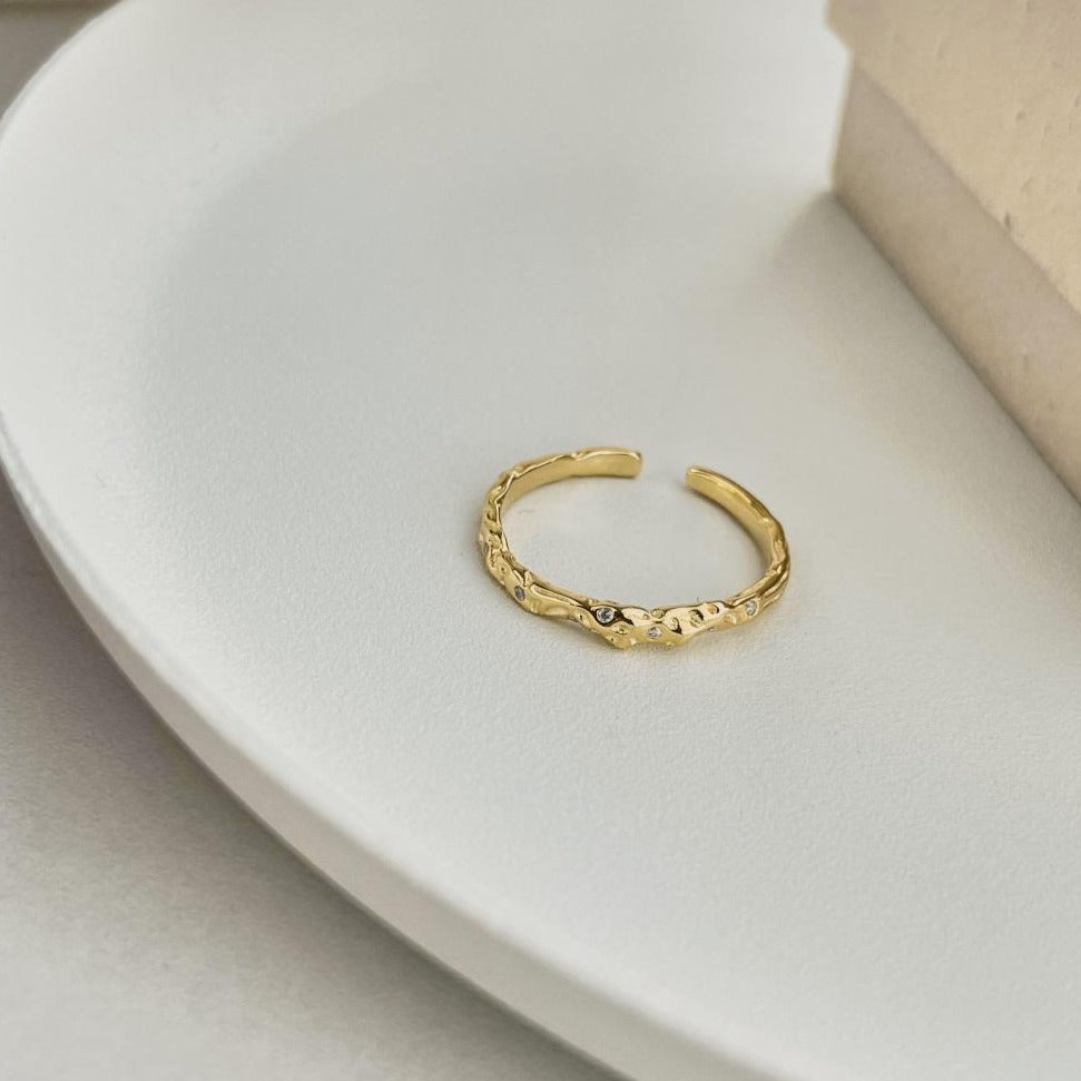 A gold-colored adjustable ring with a textured surface and embedded transparent stones.