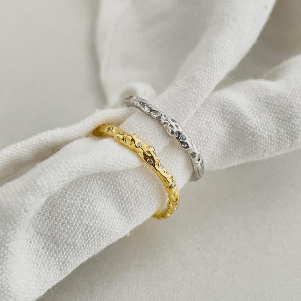 A pair of silver and gold-colored adjustable ring with a textured surface and embedded transparent stones.
