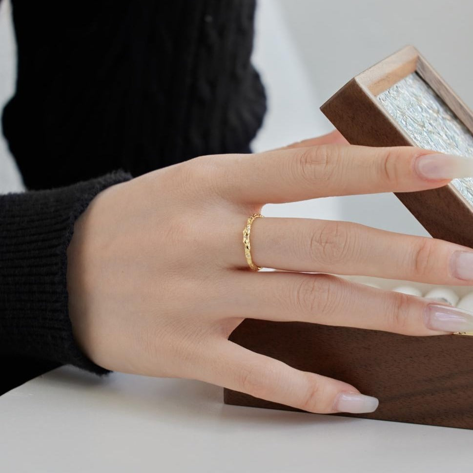 A gold-colored adjustable ring with a textured surface and embedded transparent stones.