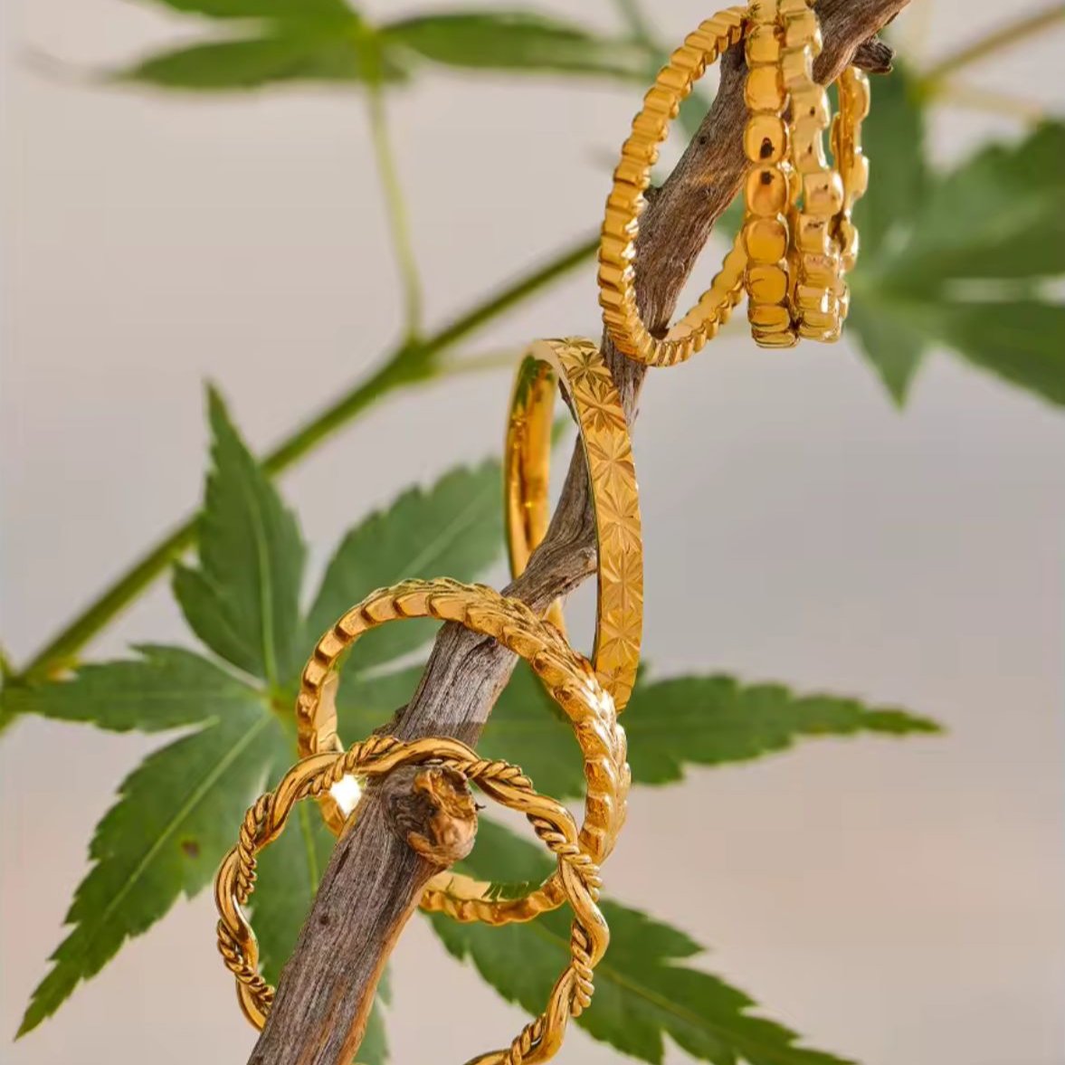 A collection of gold-plated stainless steel thin index finger cast rings with a braided design, displayed on a tree branch.
