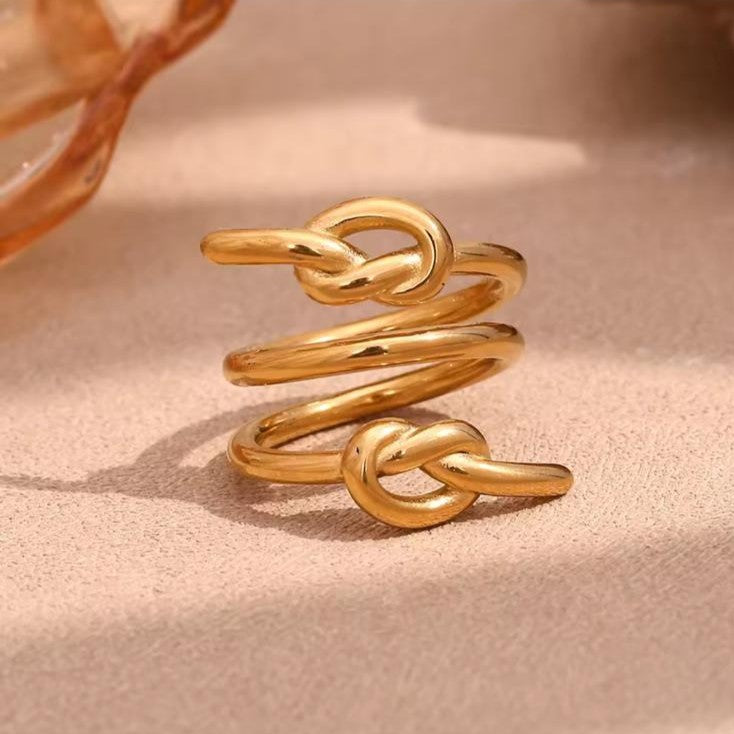 Gold knot-shaped ring on a soft pink background