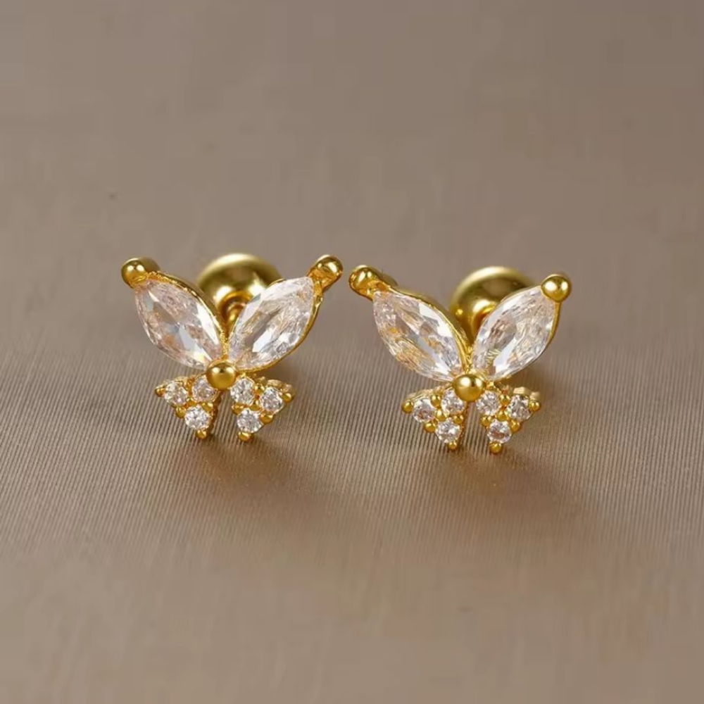 Gold butterfly earrings with clear gemstones on a beige background