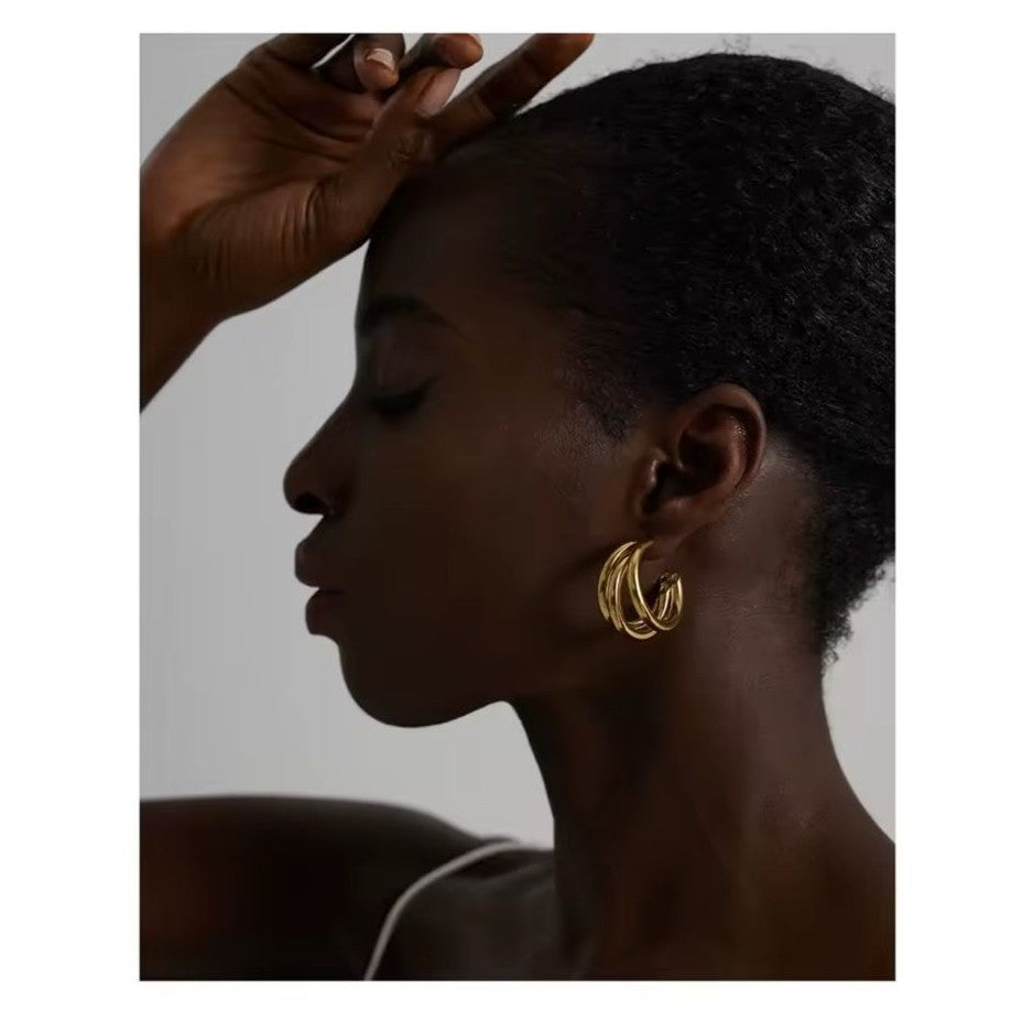 Silhouette of a person wearing gold hoop earrings with a neutral background