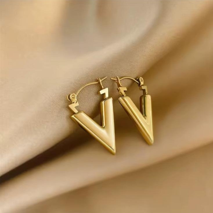 Gold V shape earrings on a beige fabric background