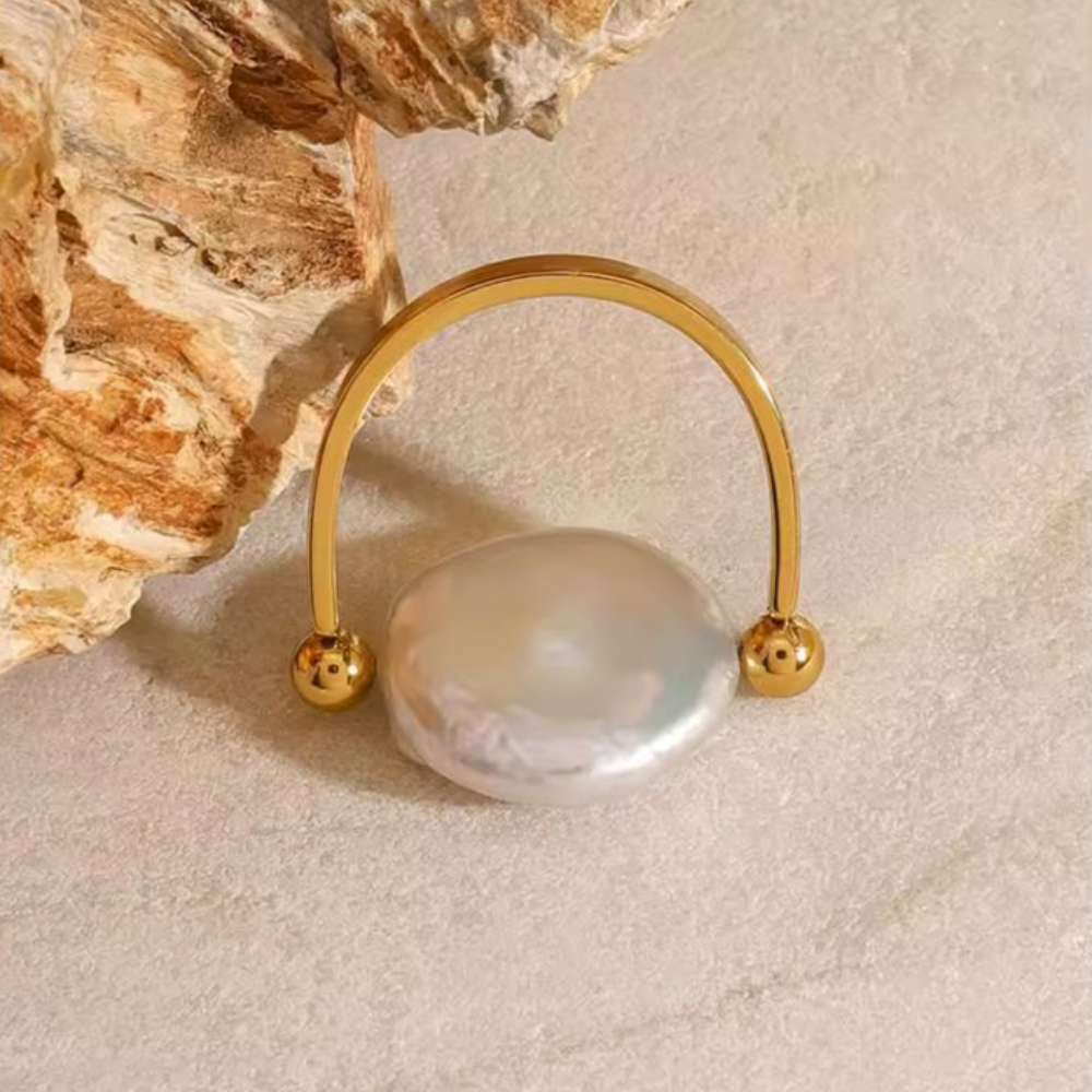 Gold ring with a pearl on a textured beige surface