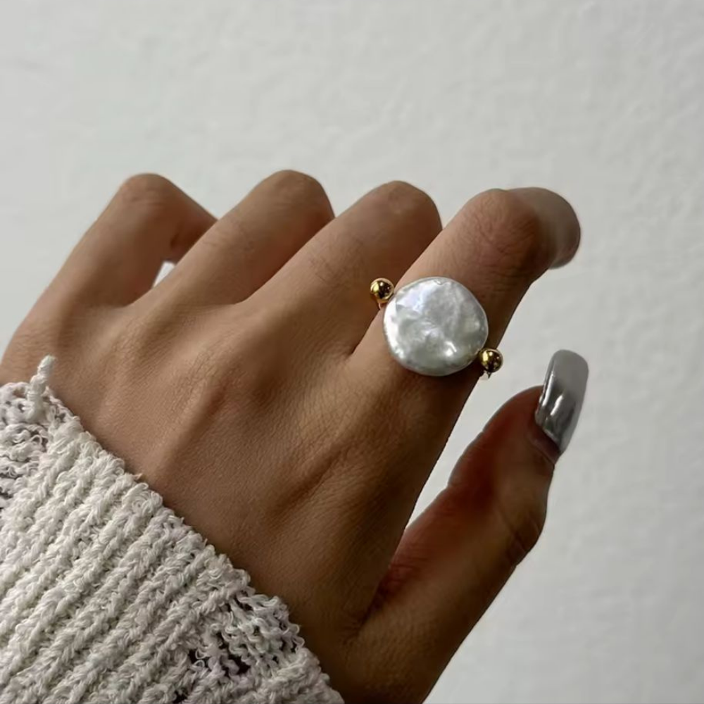 Hand wearing a large pearl ring on a plain background