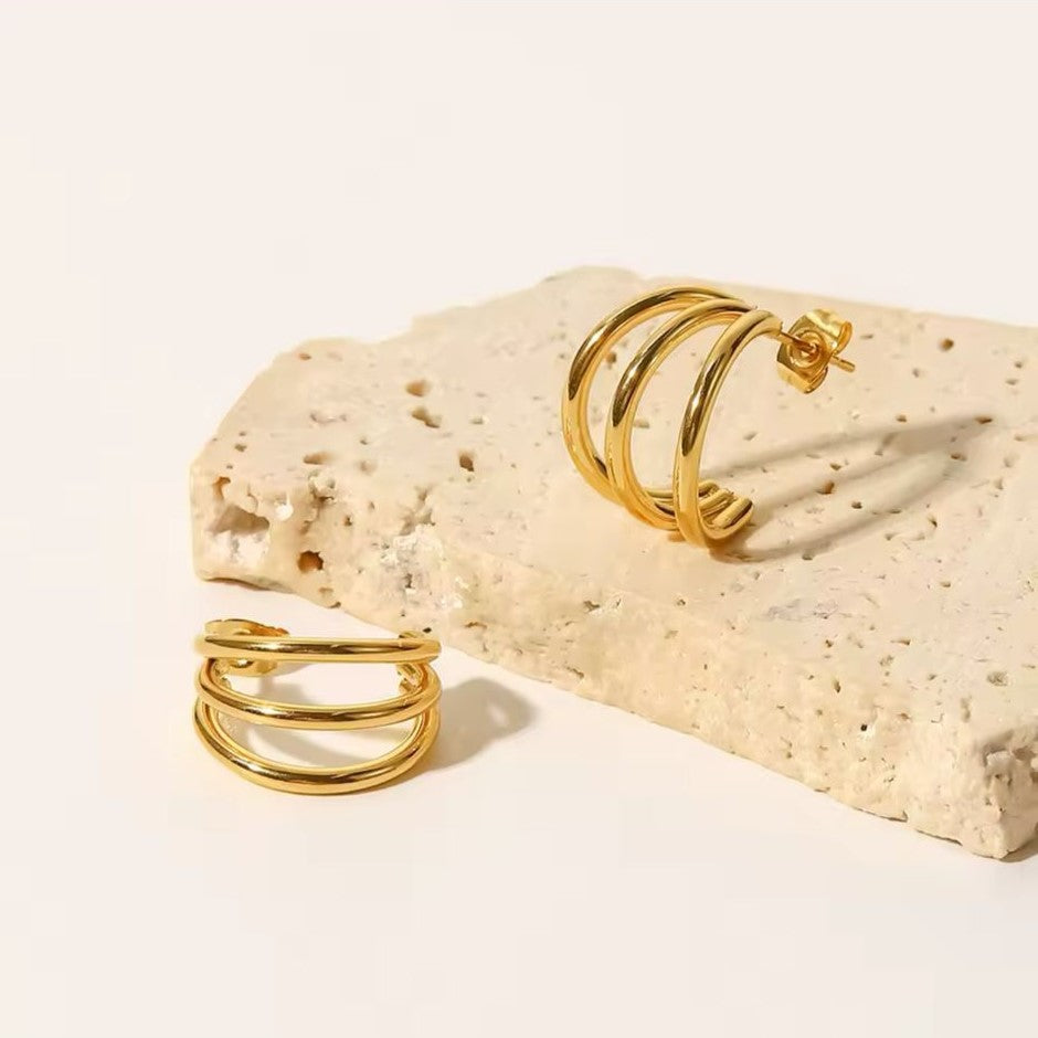 A pair of bold hoop earrings in gold-plated modern style on a white & beige background.