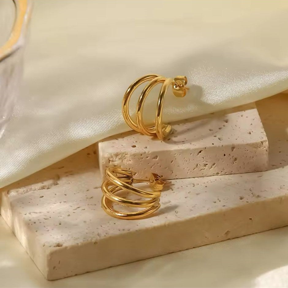 A pair of bold hoop earrings in gold-plated modern style on a white & beige background.