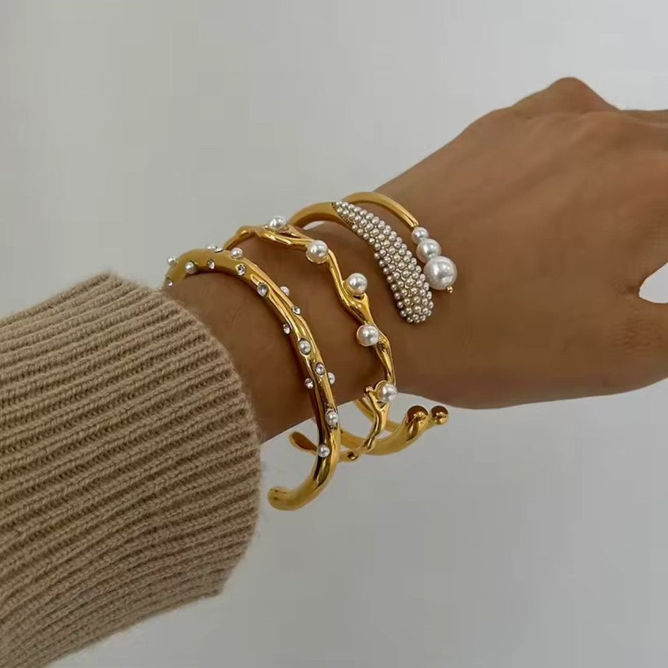 A gold-colored stainless steel bracelet with pearl adornments, displayed against a white background.