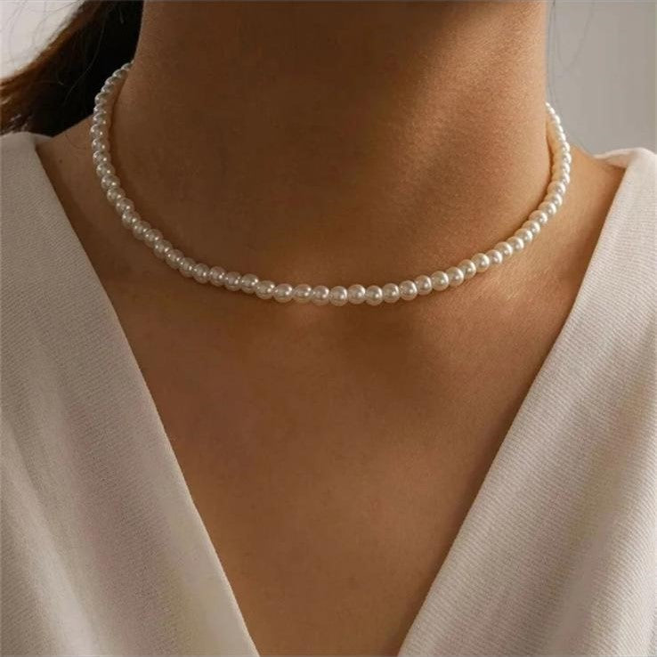 A white imitation pearl stainless steel necklace with a 14K gold finish and a length of 42+8cm presented on a women's neck.