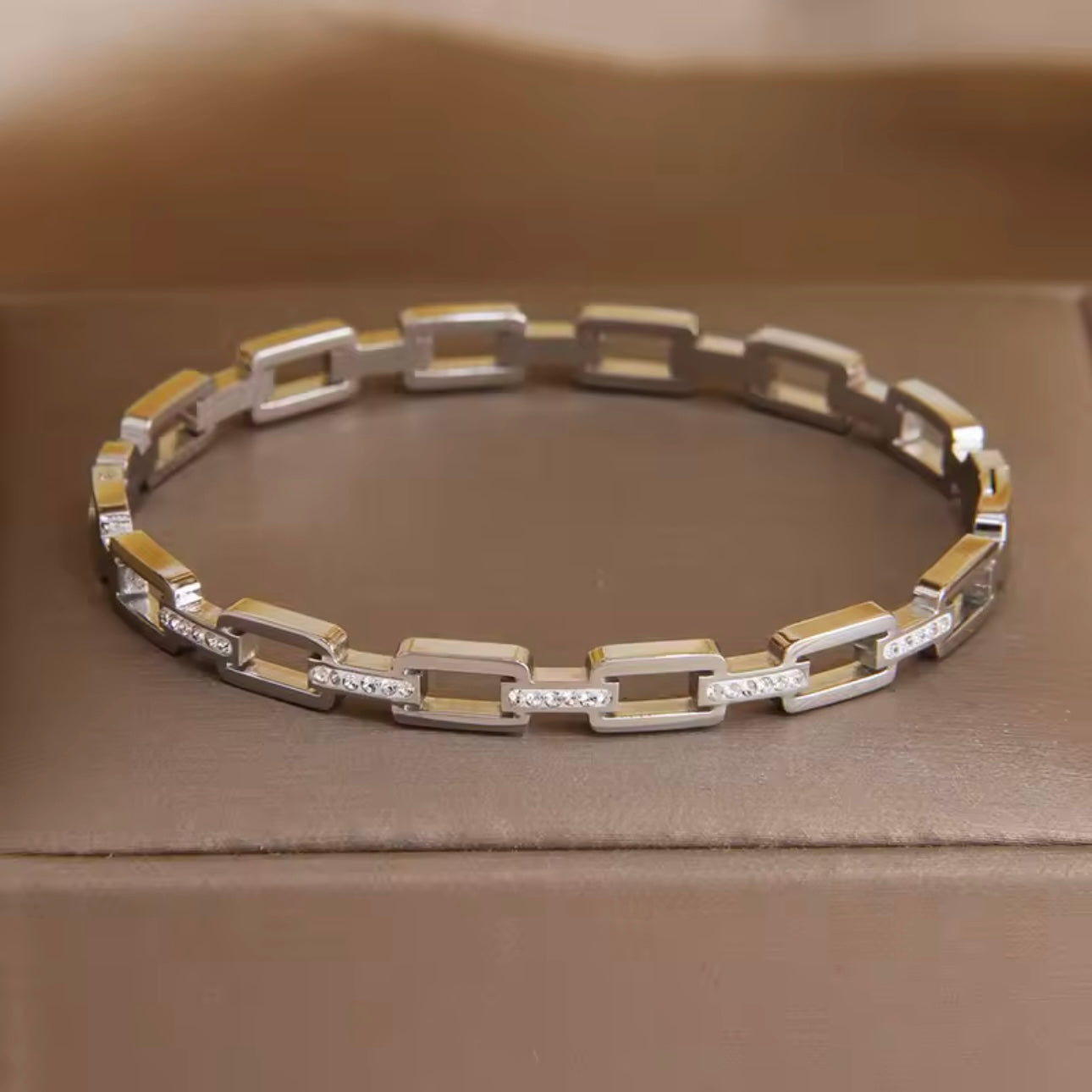A stainless steel hollow geometric bangle, with a silver finish, displayed on a textured fabric surface.