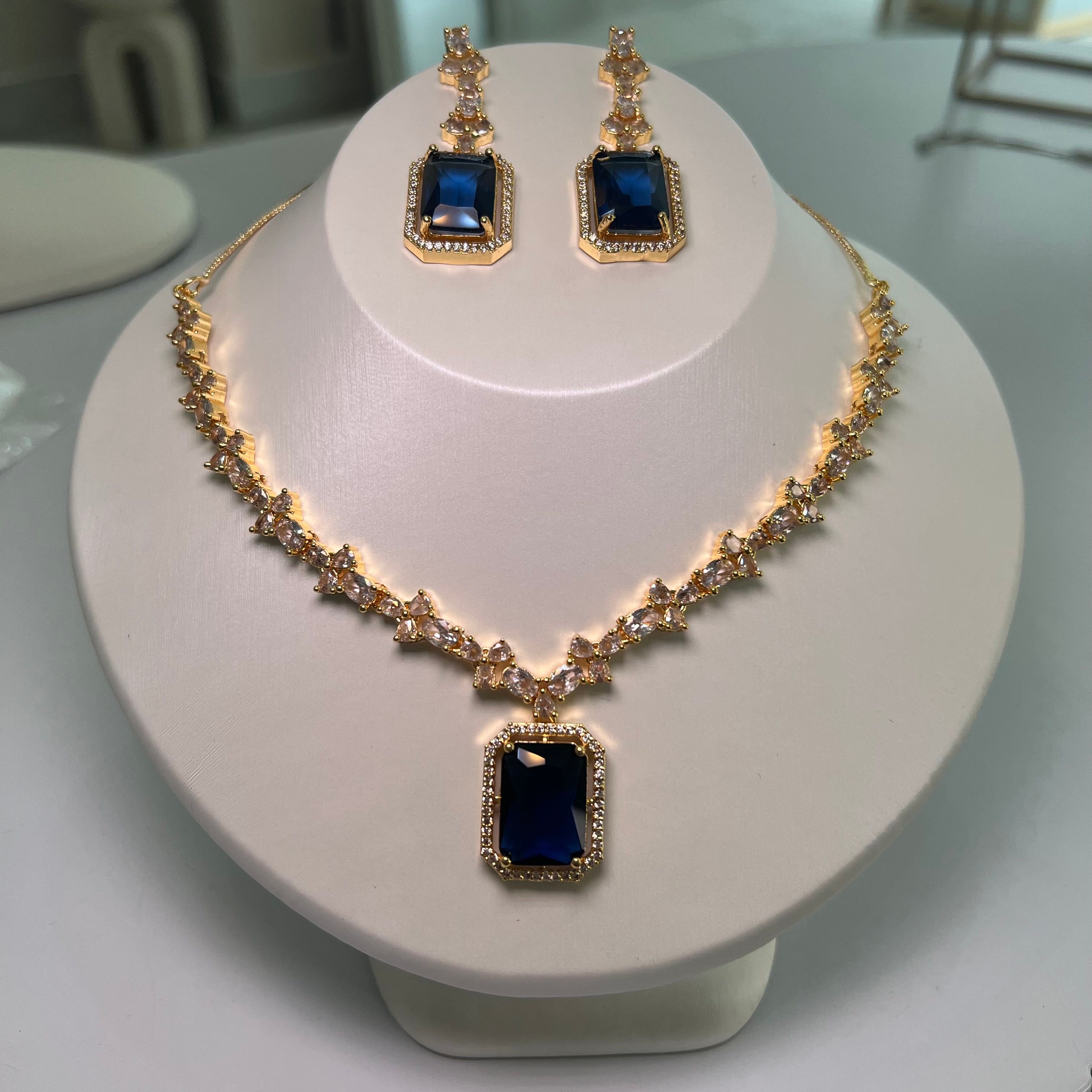A gold-tone crystal charm necklace and earrings set with a rectangular centerpiece and drop earrings on a mannequin.