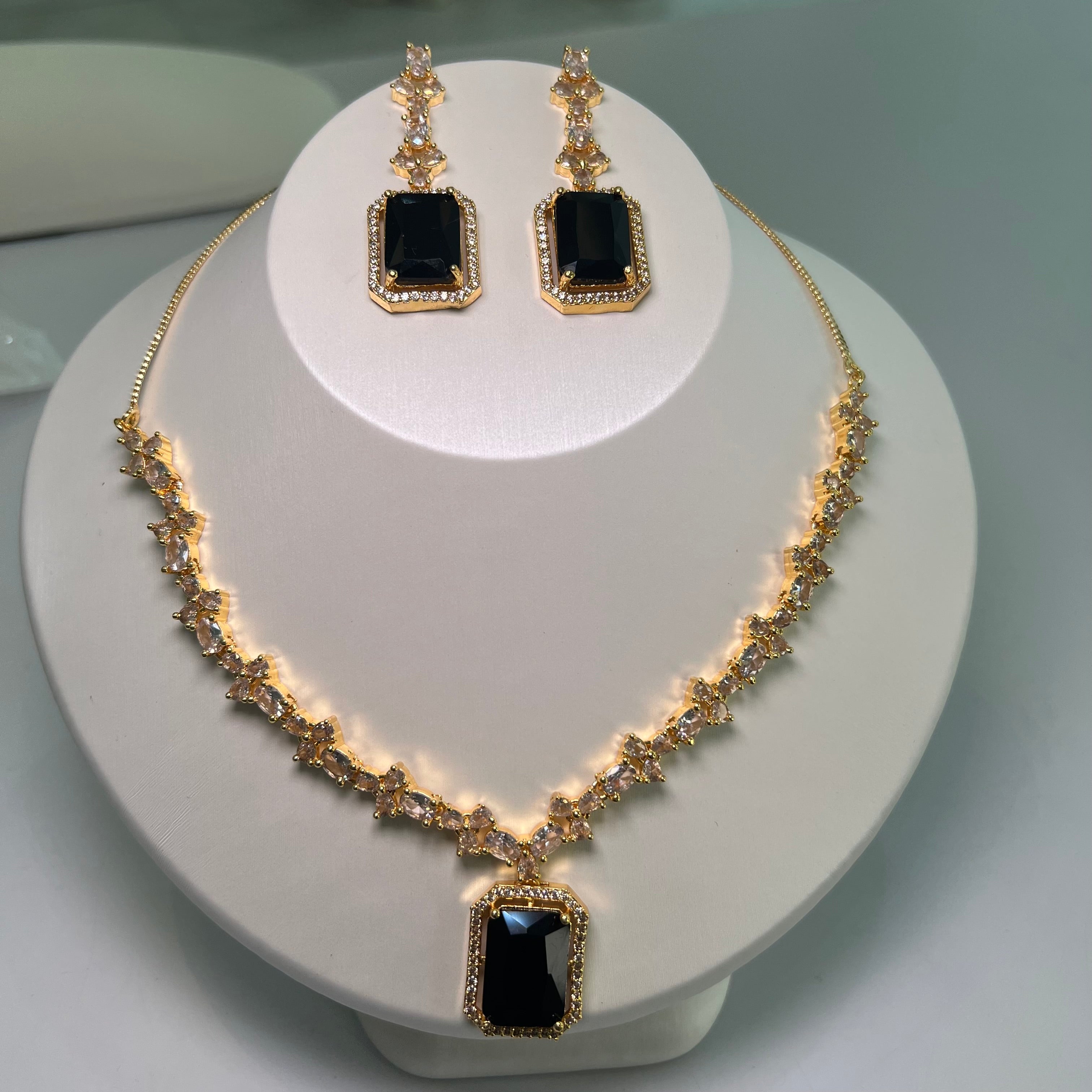 A gold-tone crystal charm necklace and earrings set with a rectangular centerpiece and drop earrings on a mannequin.