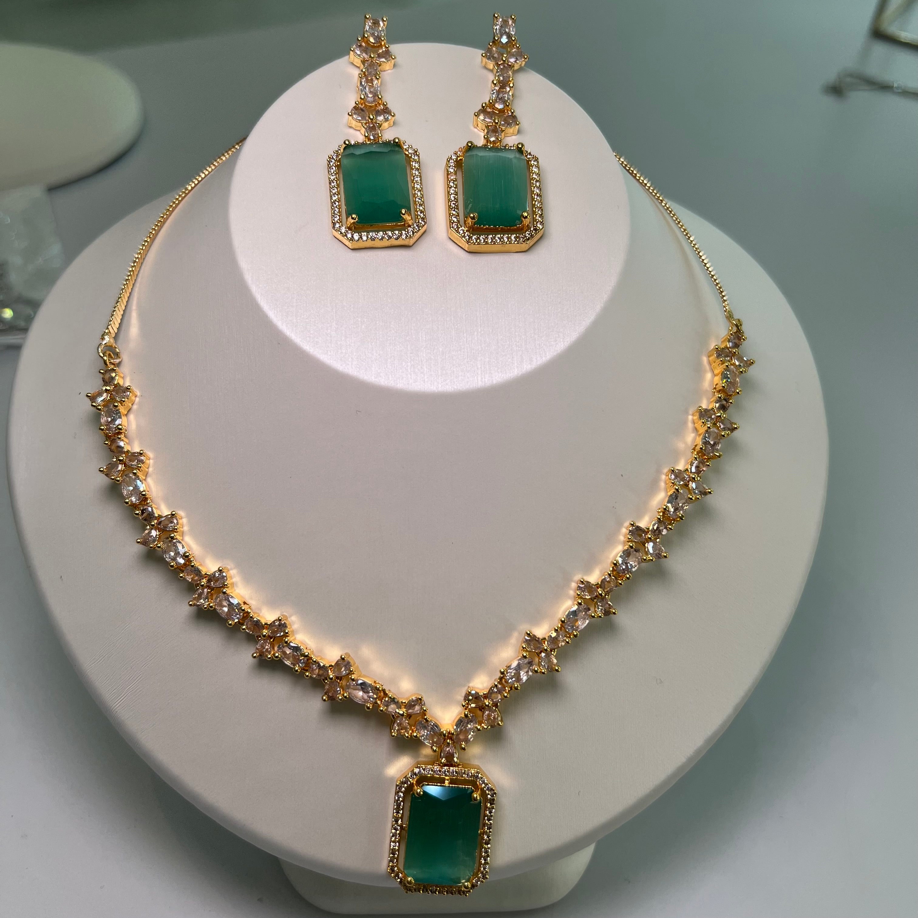 A gold-tone crystal charm necklace and earrings set with a rectangular centerpiece and drop earrings on a mannequin.