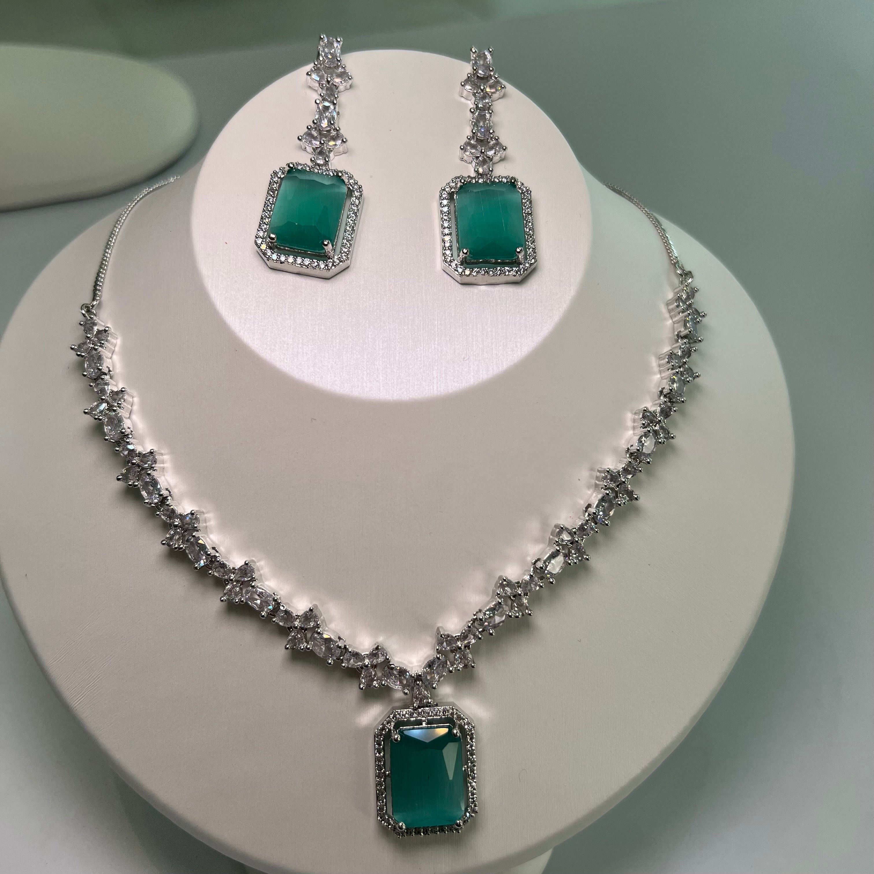 A silver-tone crystal charm necklace and earrings set with a rectangular centerpiece and drop earrings on a mannequin.