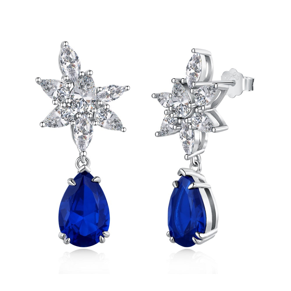 A pair of silver drop earrings featuring pear-shaped blue stones with intricate floral designs above the earrings.