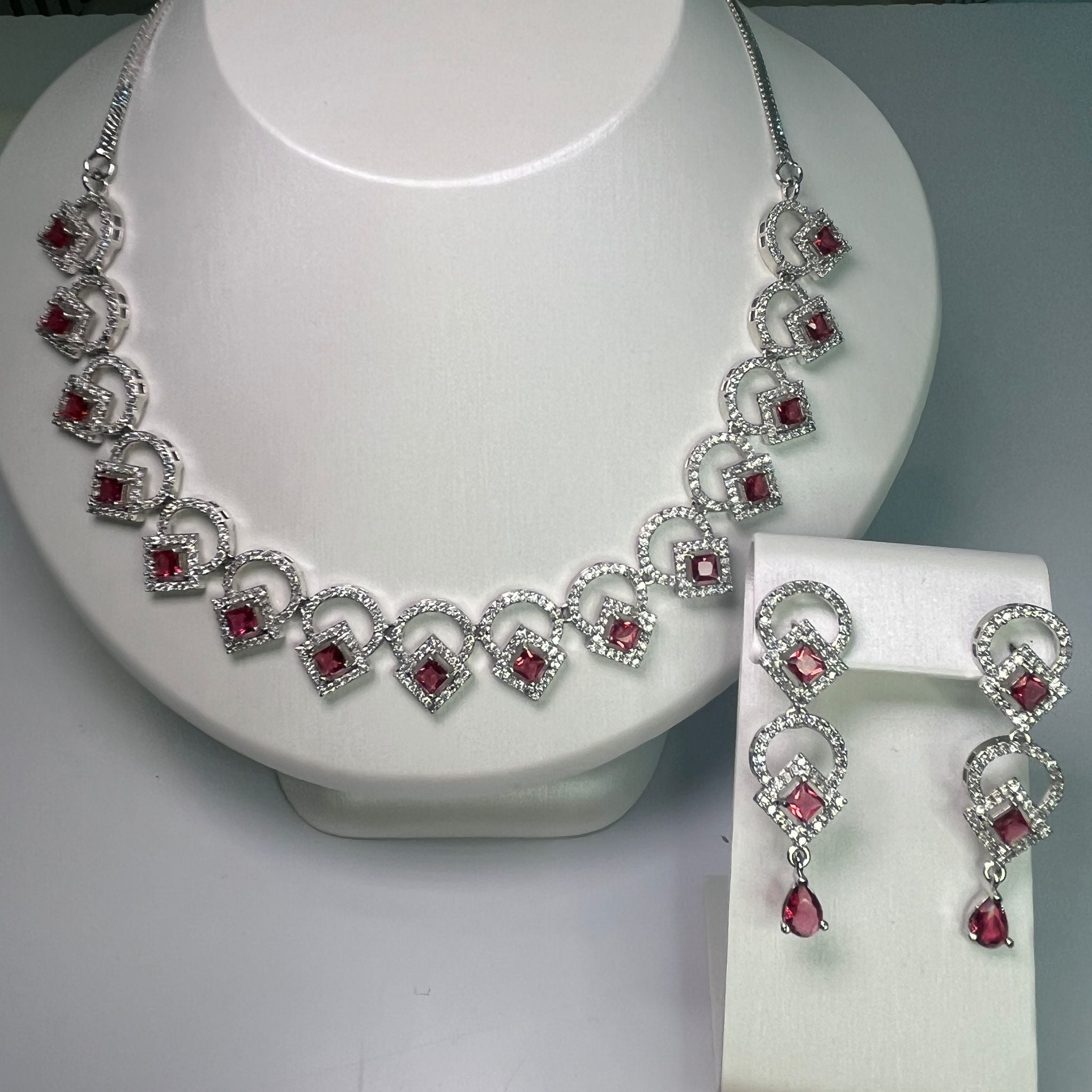 A jewelry set showcasing a wave-like necklace and matching earrings, adorned with pink crystals, displayed on a white mannequin bust.
