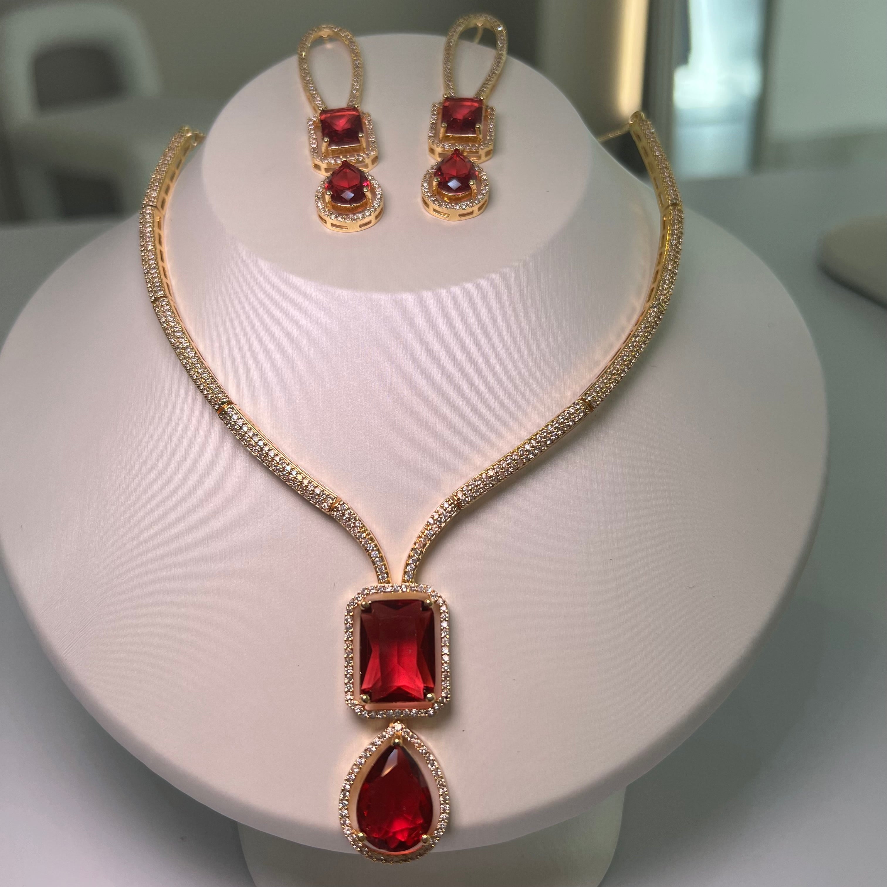 A gold-tone Empire Drape Necklace and Earrings set with red gemstone pendants displayed on a mannequin bust