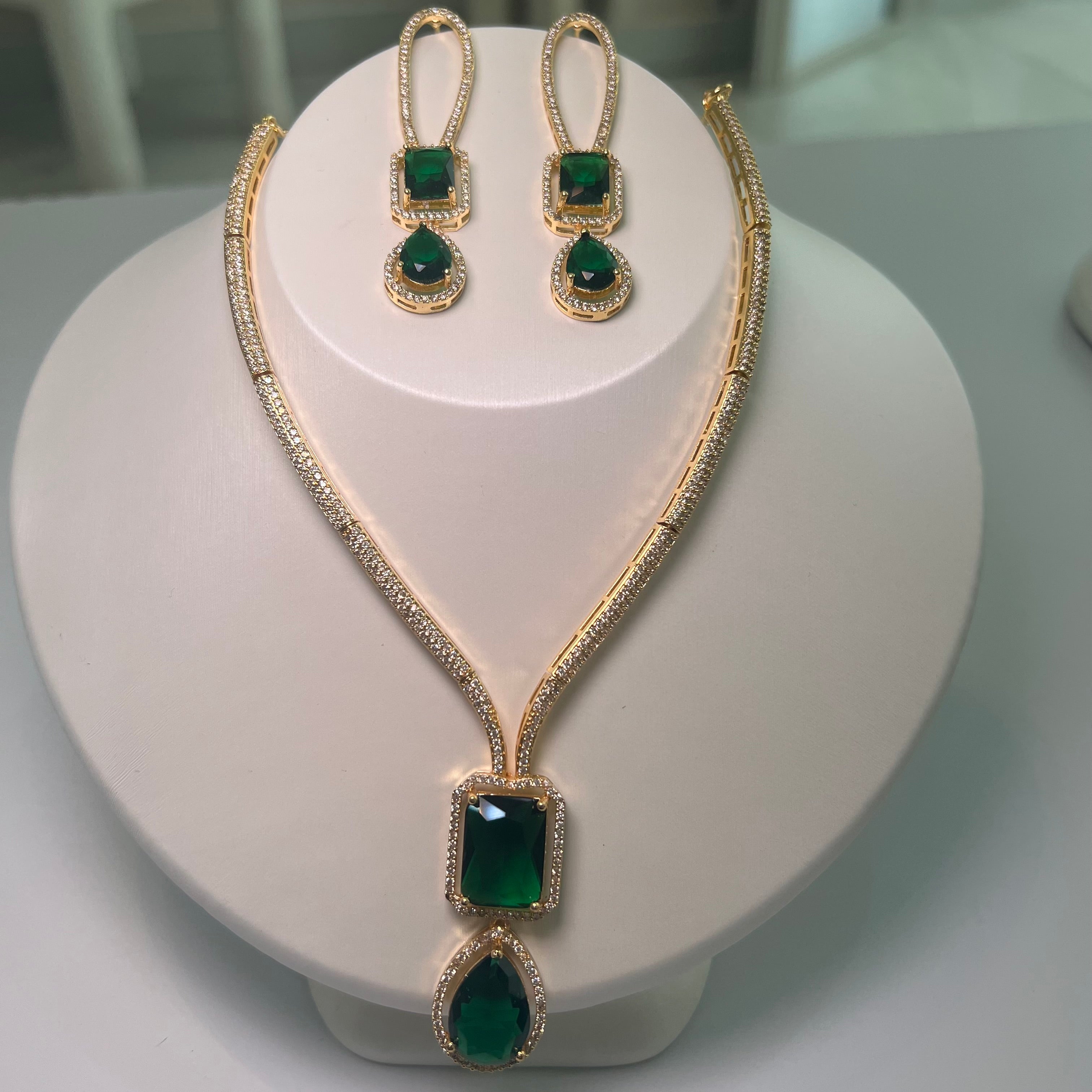 A gold-tone Empire Drape Necklace and Earrings set with green gemstone pendants displayed on a mannequin bust