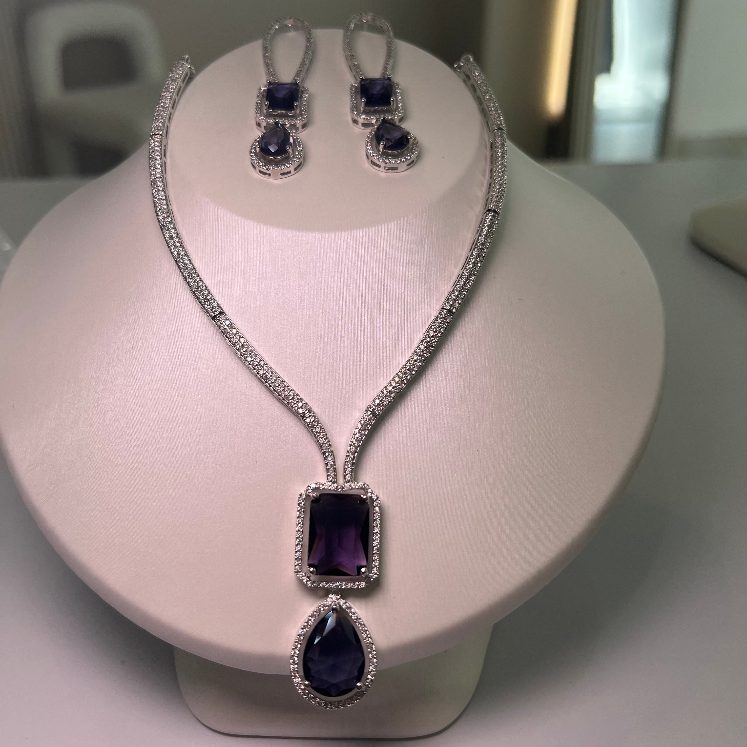 A silver-tone Empire Drape Necklace and Earrings set with purple gemstone pendants displayed on a mannequin bust