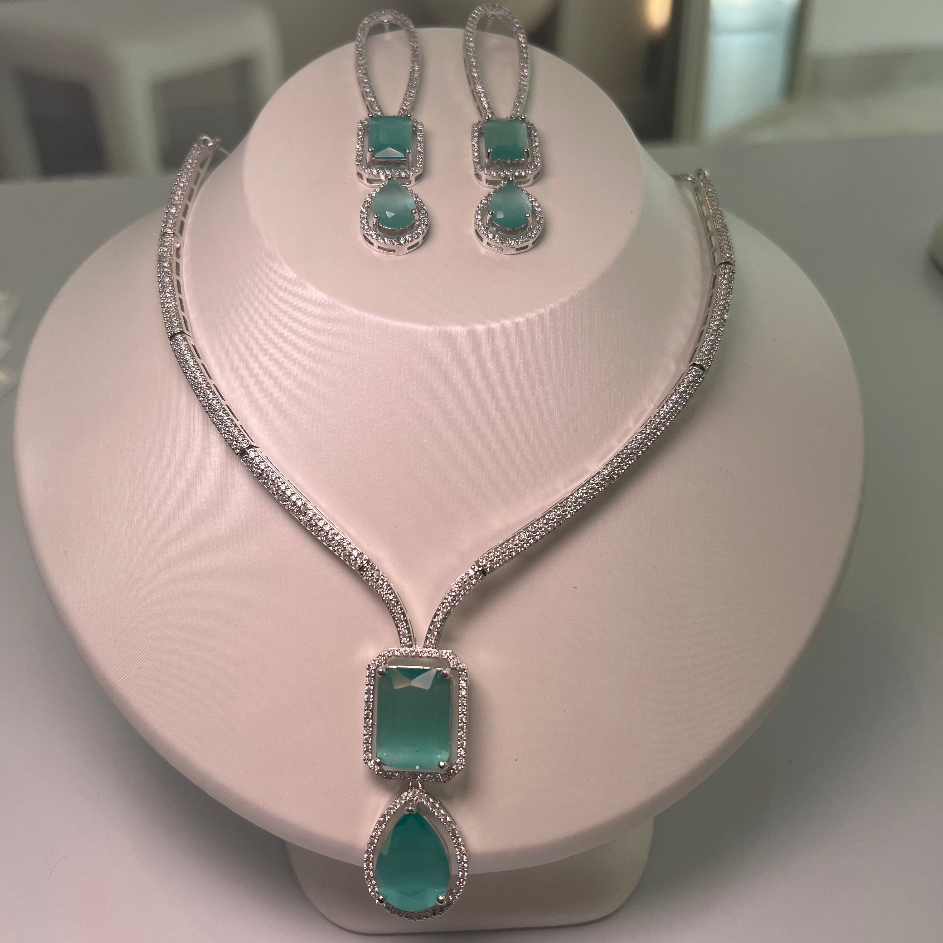A silver-tone Empire Drape Necklace and Earrings set with dive-blue gemstone pendants displayed on a mannequin bust