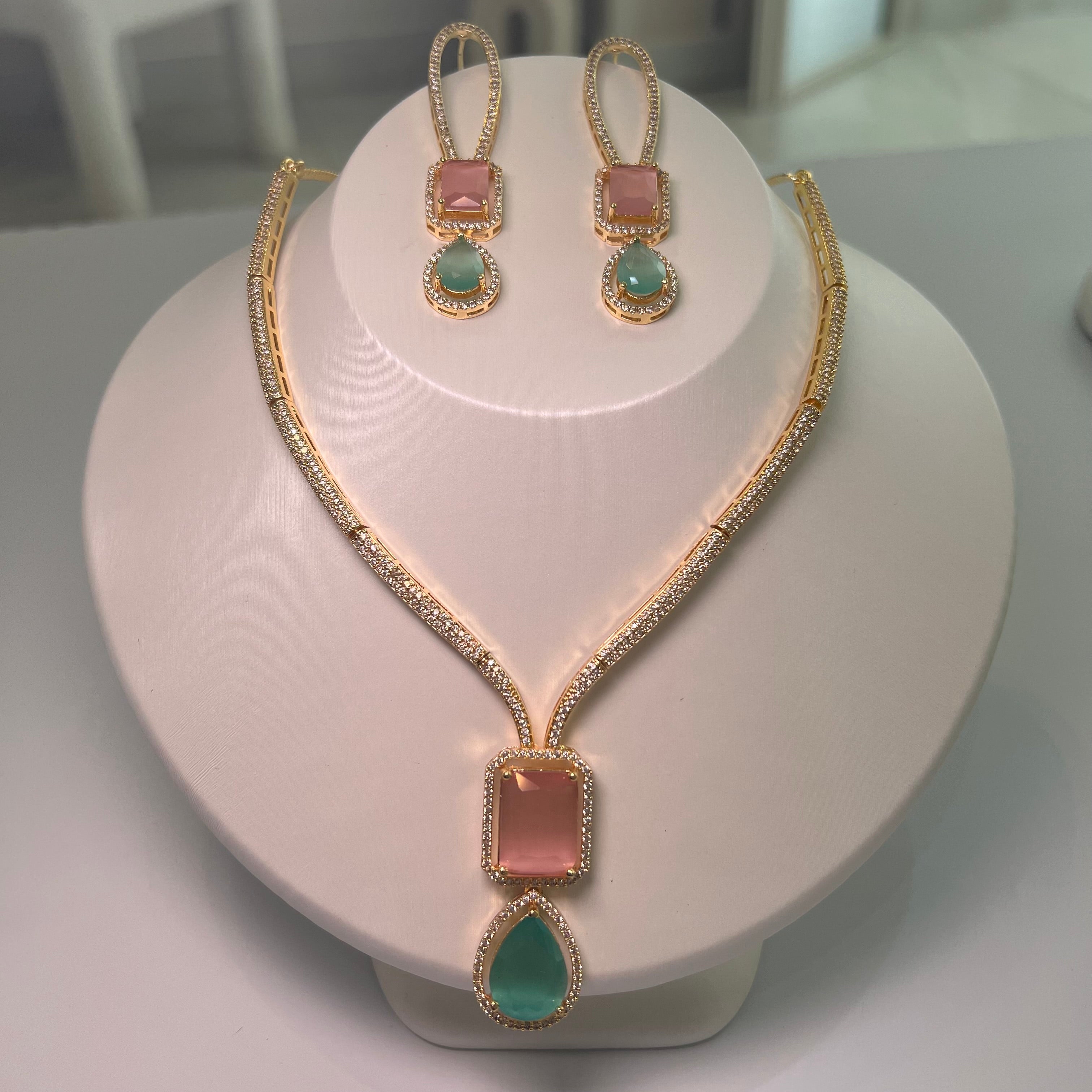 A gold-tone Empire Drape Necklace and Earrings set with pink and green gemstone pendants displayed on a mannequin bust