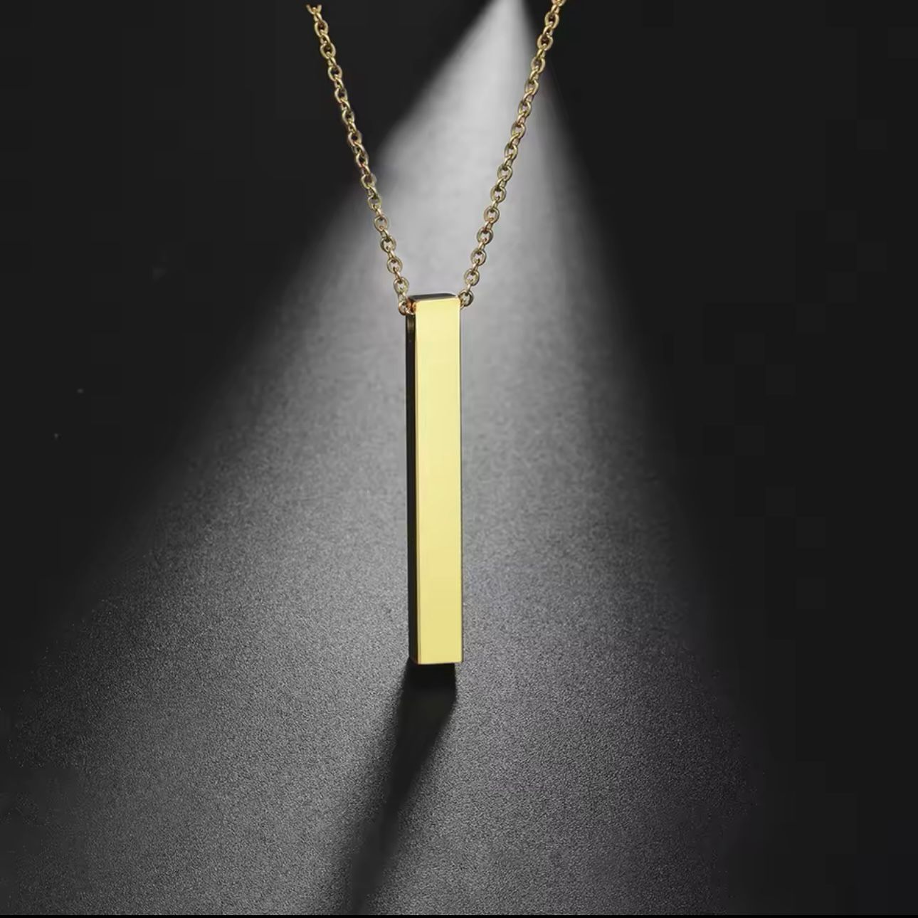 A gold-plated bar necklace with engraved names on it, displayed on a grey background.