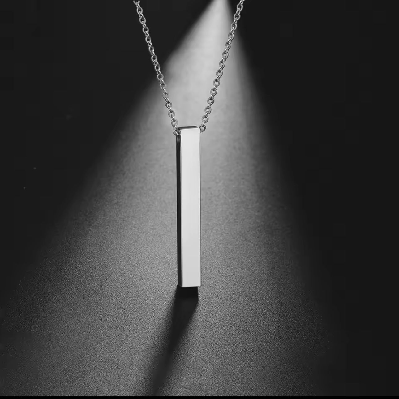 A gold-plated bar necklace with engraved names on it, displayed on a grey background.