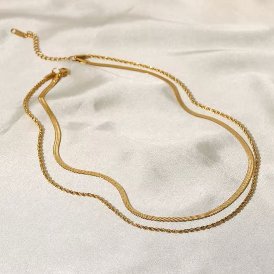 A gold colored twin chain necklace displayed over white fabric in the background.