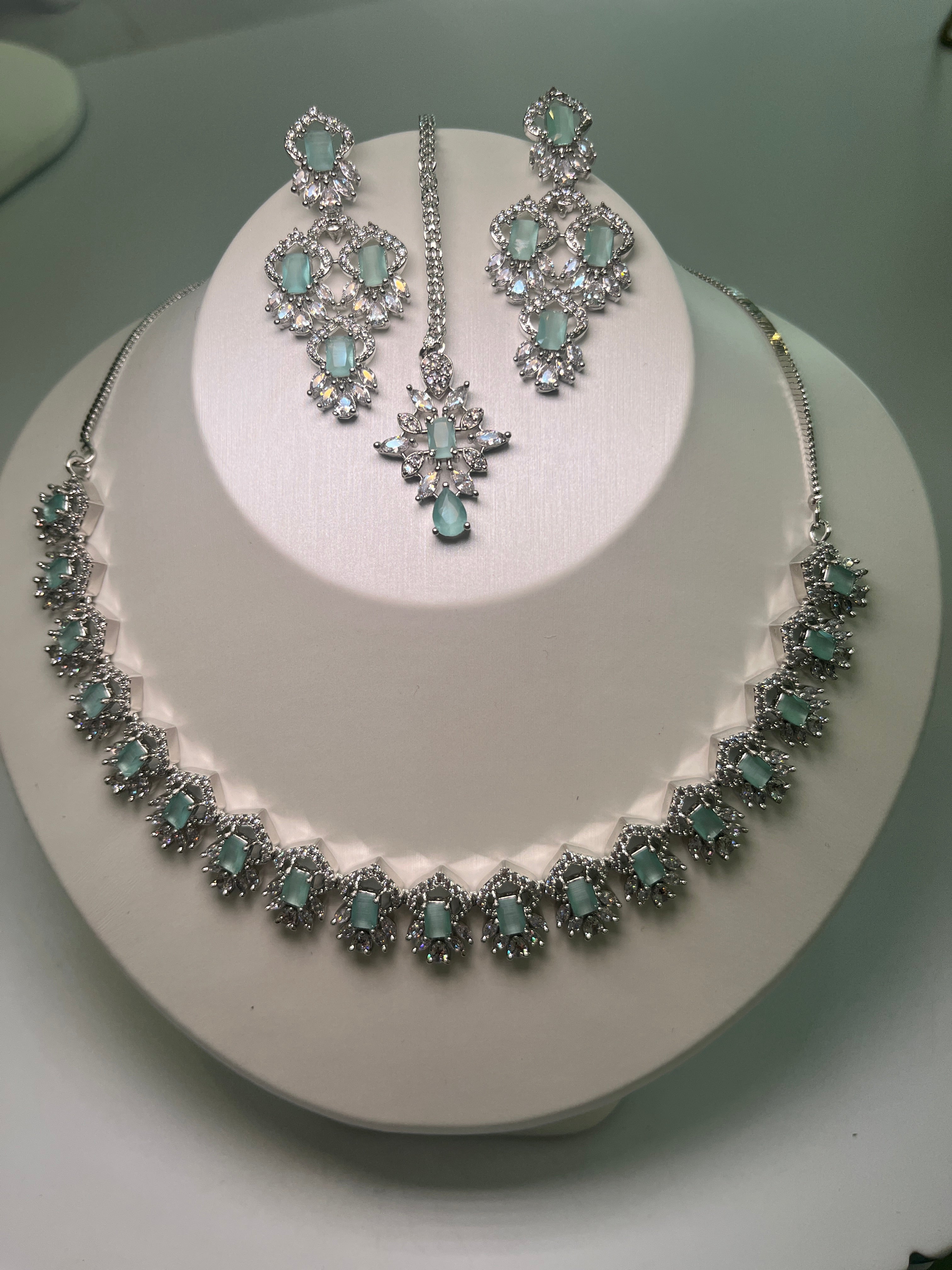 A necklace and earrings set with baguette-cut gemstones and brilliant crystals displayed on a mannequin.