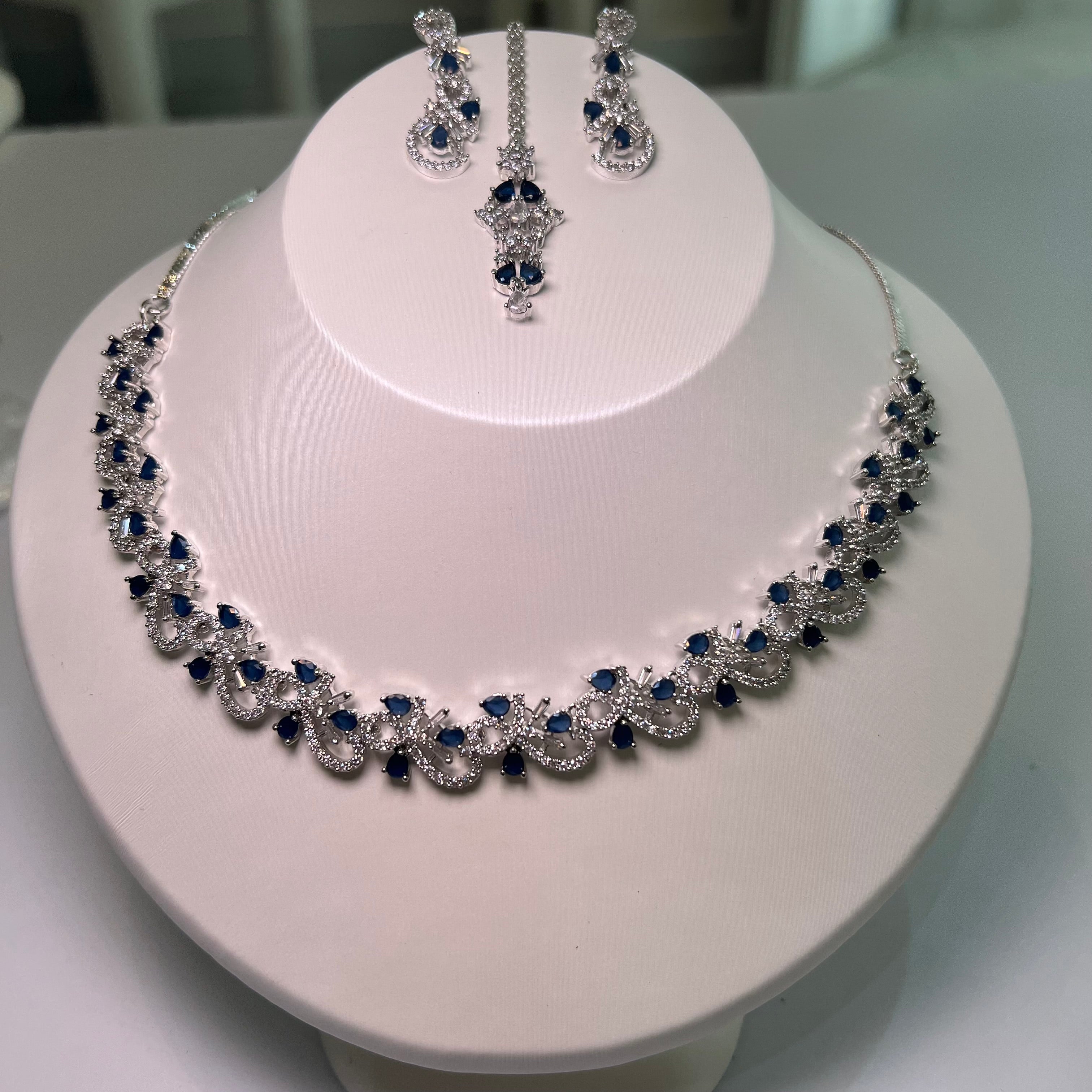 A necklace and earrings set displayed on a mannequin, featuring silver-tone chains with floral-inspired patterns and blue stones.