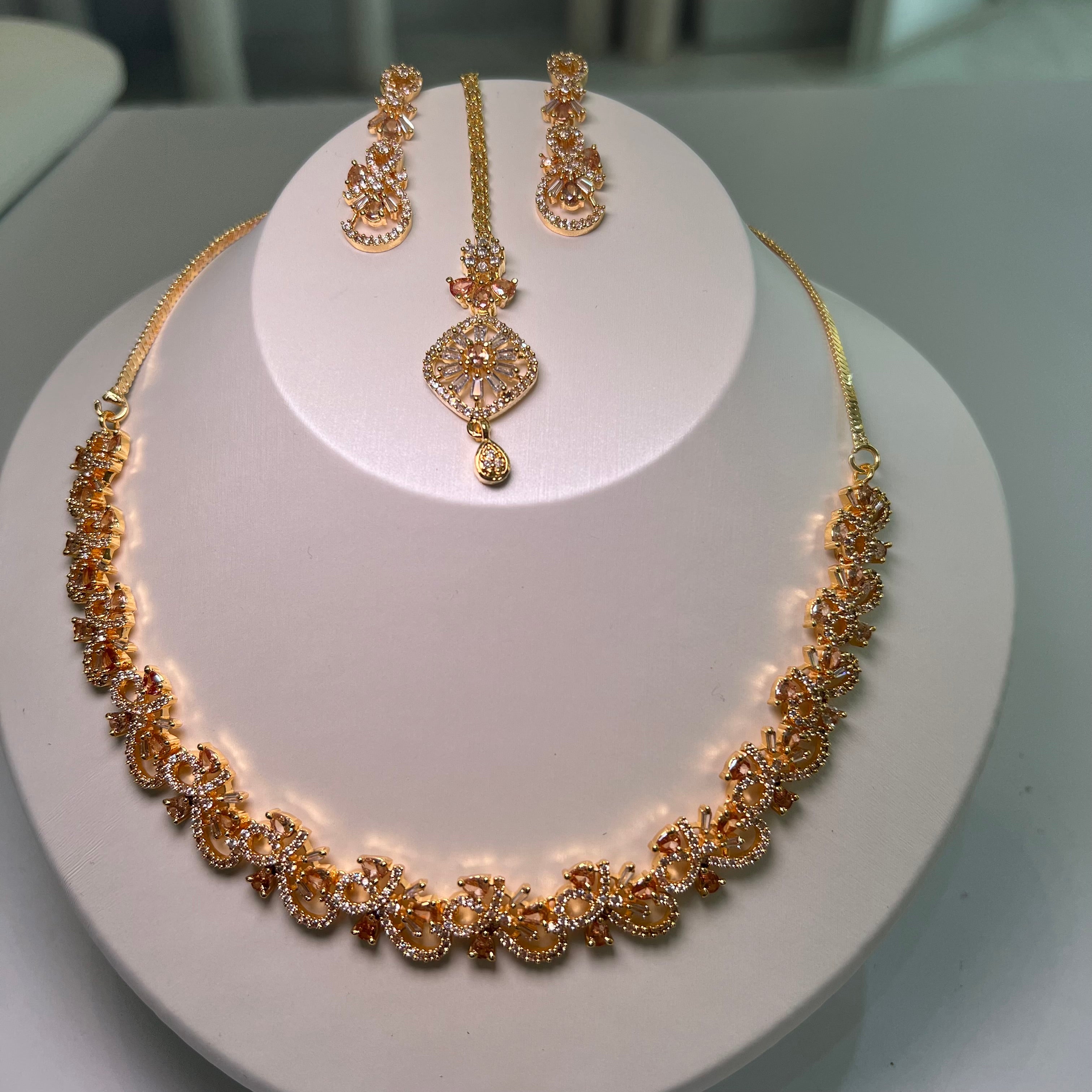 A necklace and earrings set displayed on a mannequin, featuring gold-tone chains with floral-inspired patterns and multicolored stones.