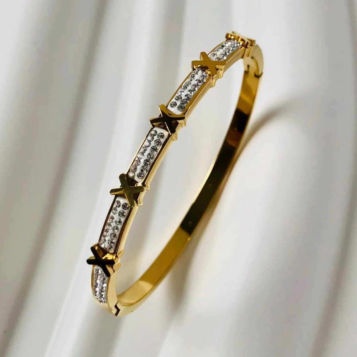 A gold stainless steel bangle bracelet with intricate designs and sparkling accents.