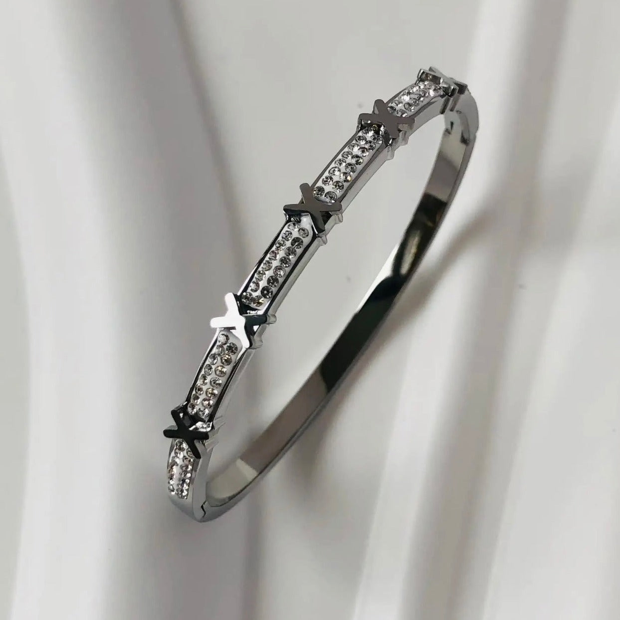 A silver stainless steel bangle bracelet with intricate designs and sparkling accents.